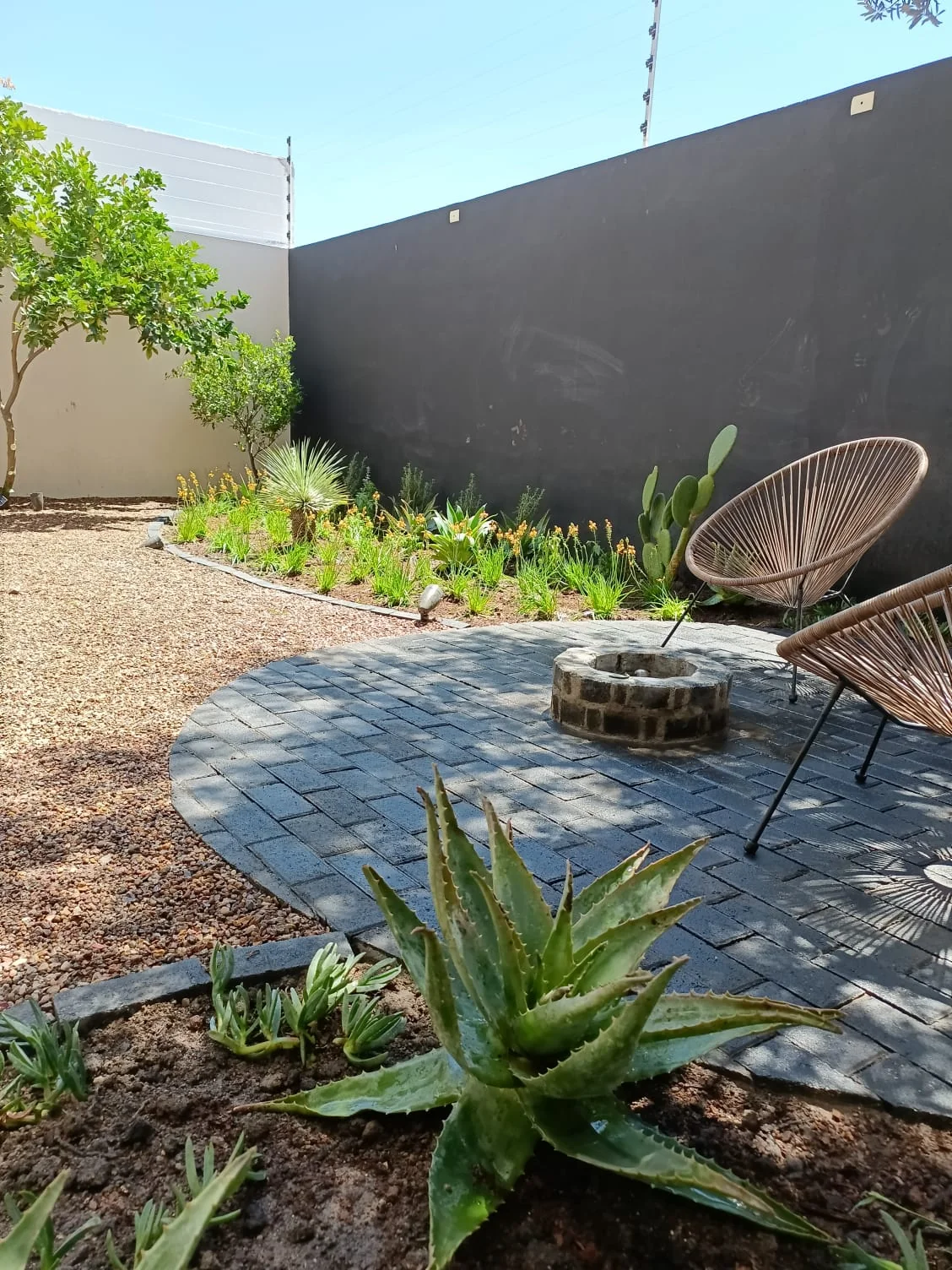Patio con asientos alrededor de un fogatero y vegetación